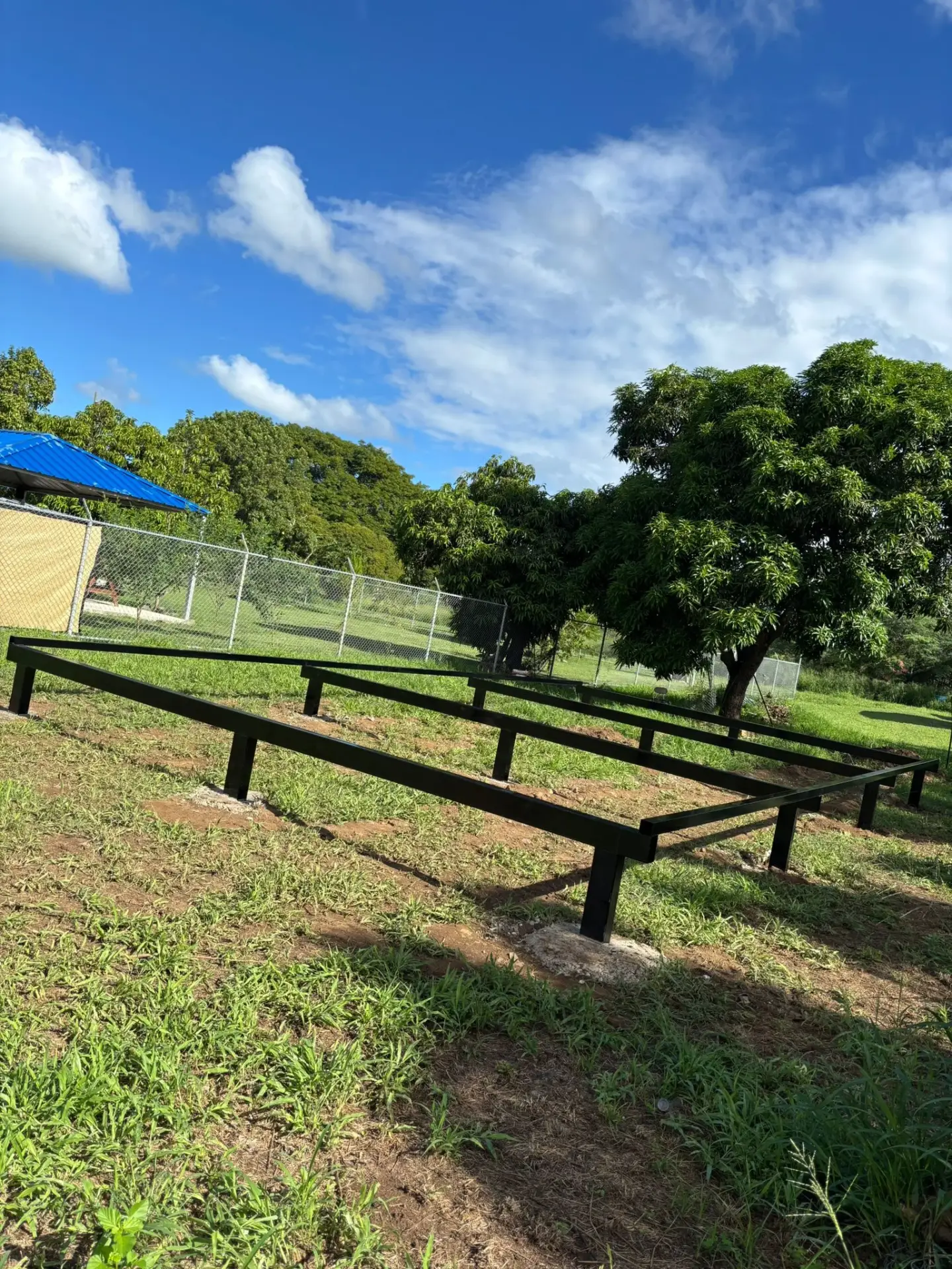 Black steel foundation frame installed on a grassy tropical lot beneath a blue sky
