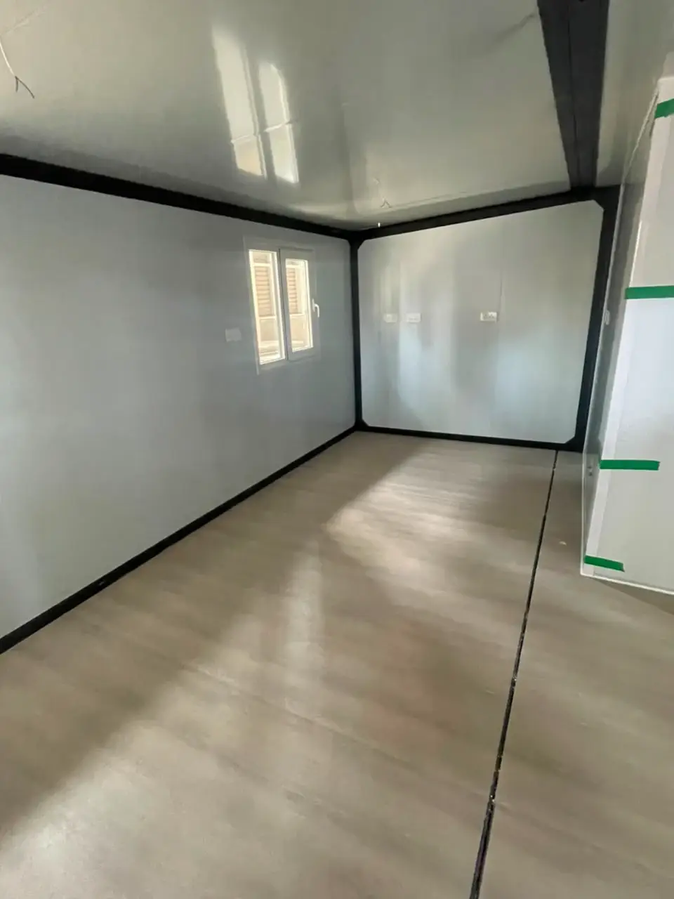 Empty gray modular-home room with black framing and unfinished ceiling wiring