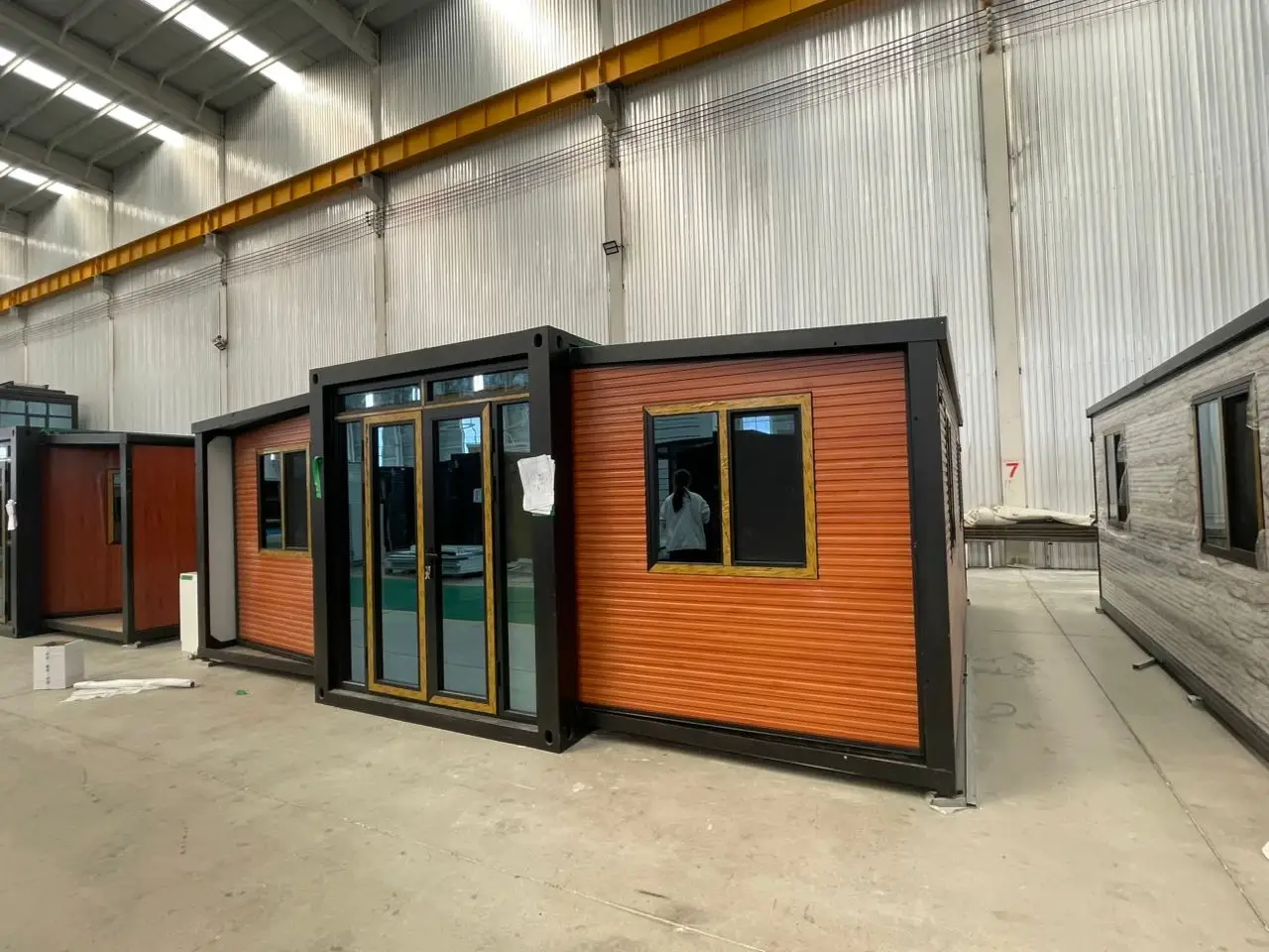 Orange-clad modular building unit under assembly inside a factory