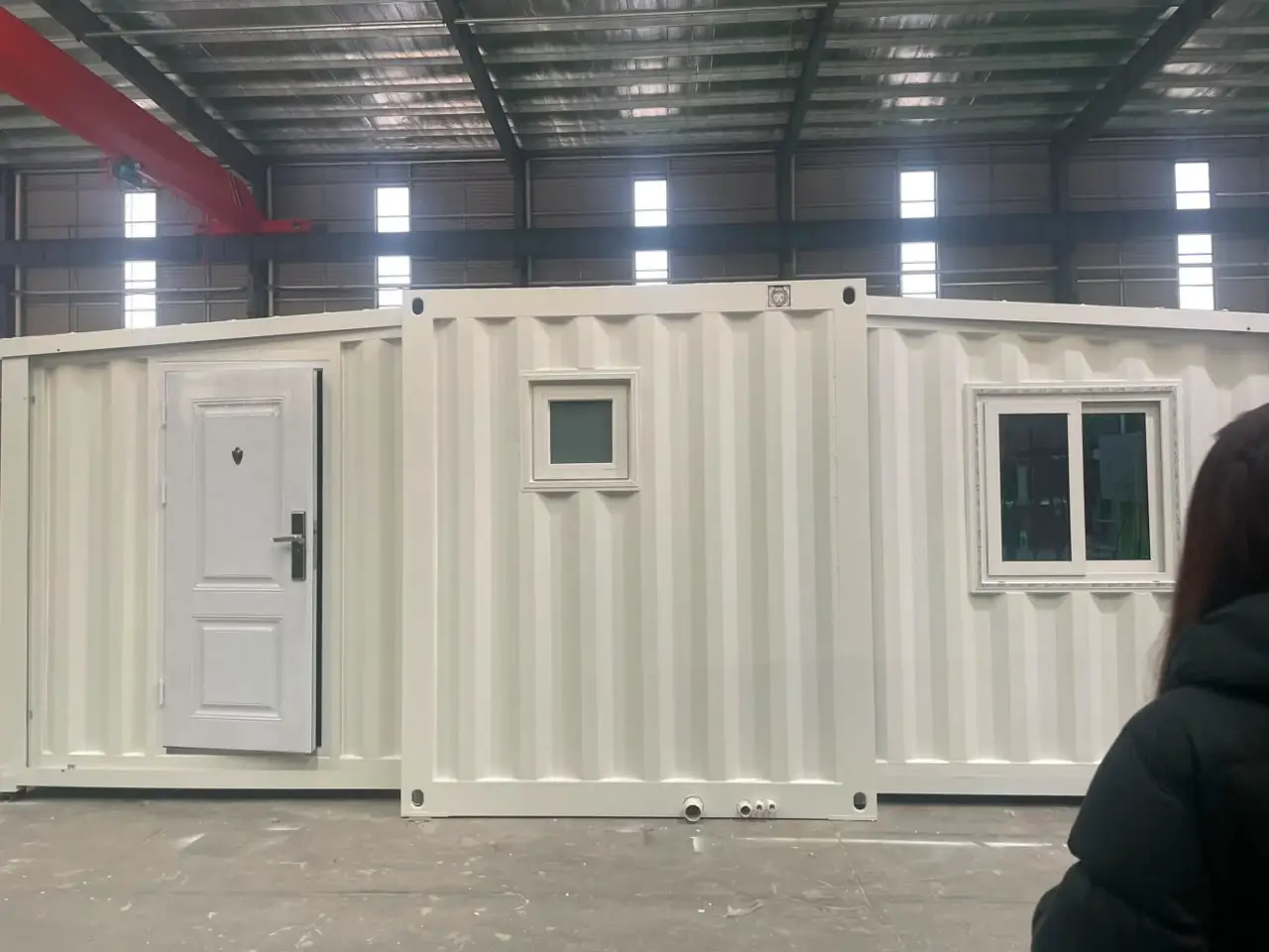 White container-style modular unit with a paneled door and windows inside a factory