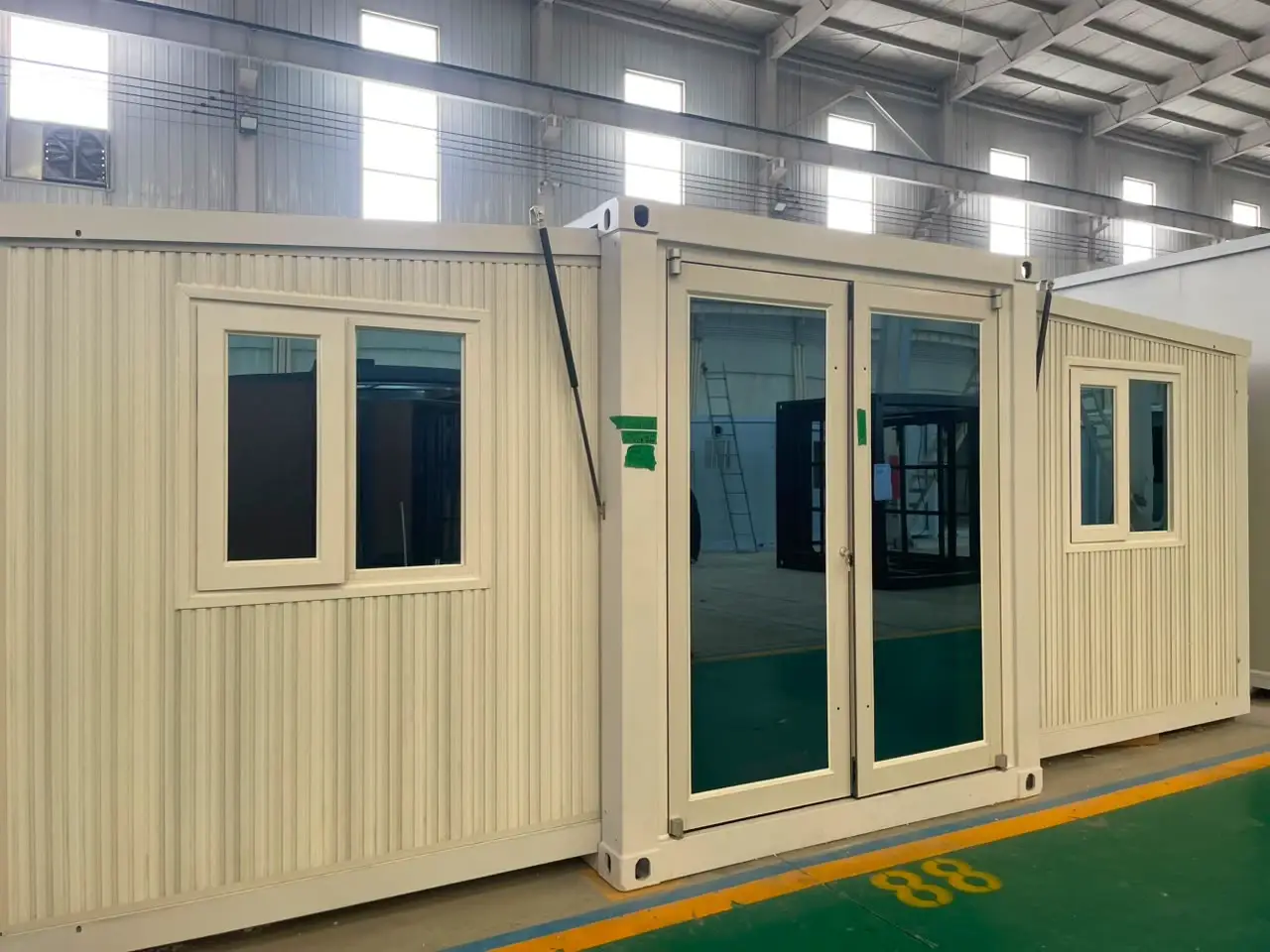 Cream expandable modular unit with central glass doors on a factory floor