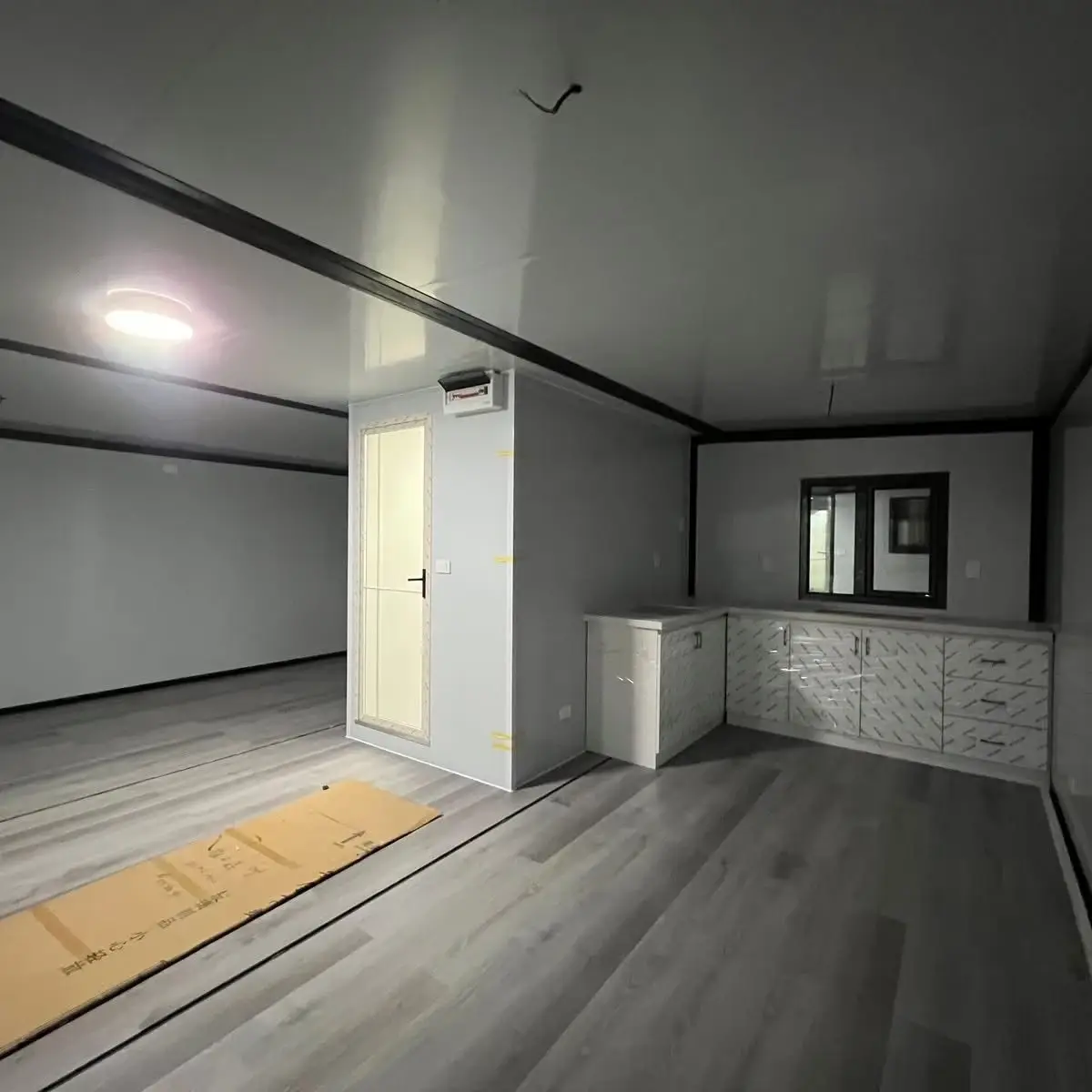 Open modular-home interior with a compact kitchen, gray flooring, and unfinished wiring