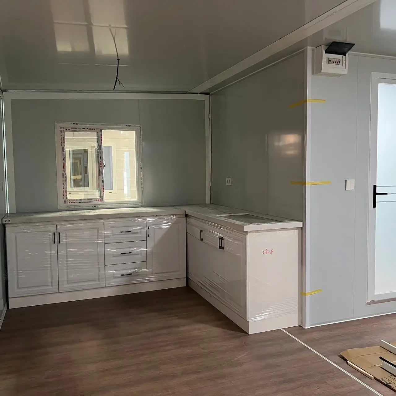 Compact modular-home kitchen with wrapped cabinets, a window, and an electrical panel