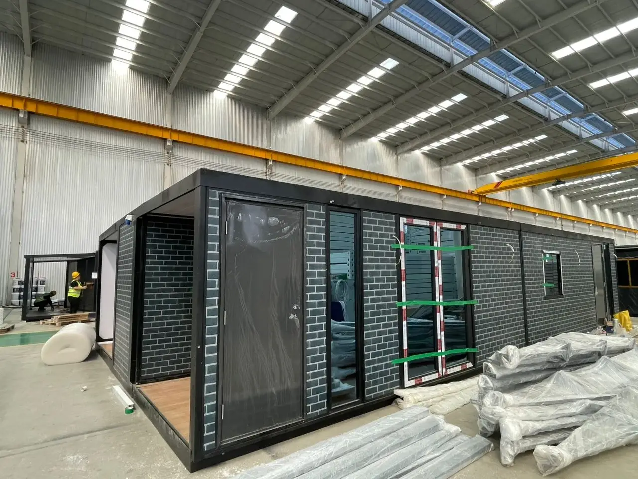 Long dark faux-brick modular unit under assembly in a manufacturing warehouse