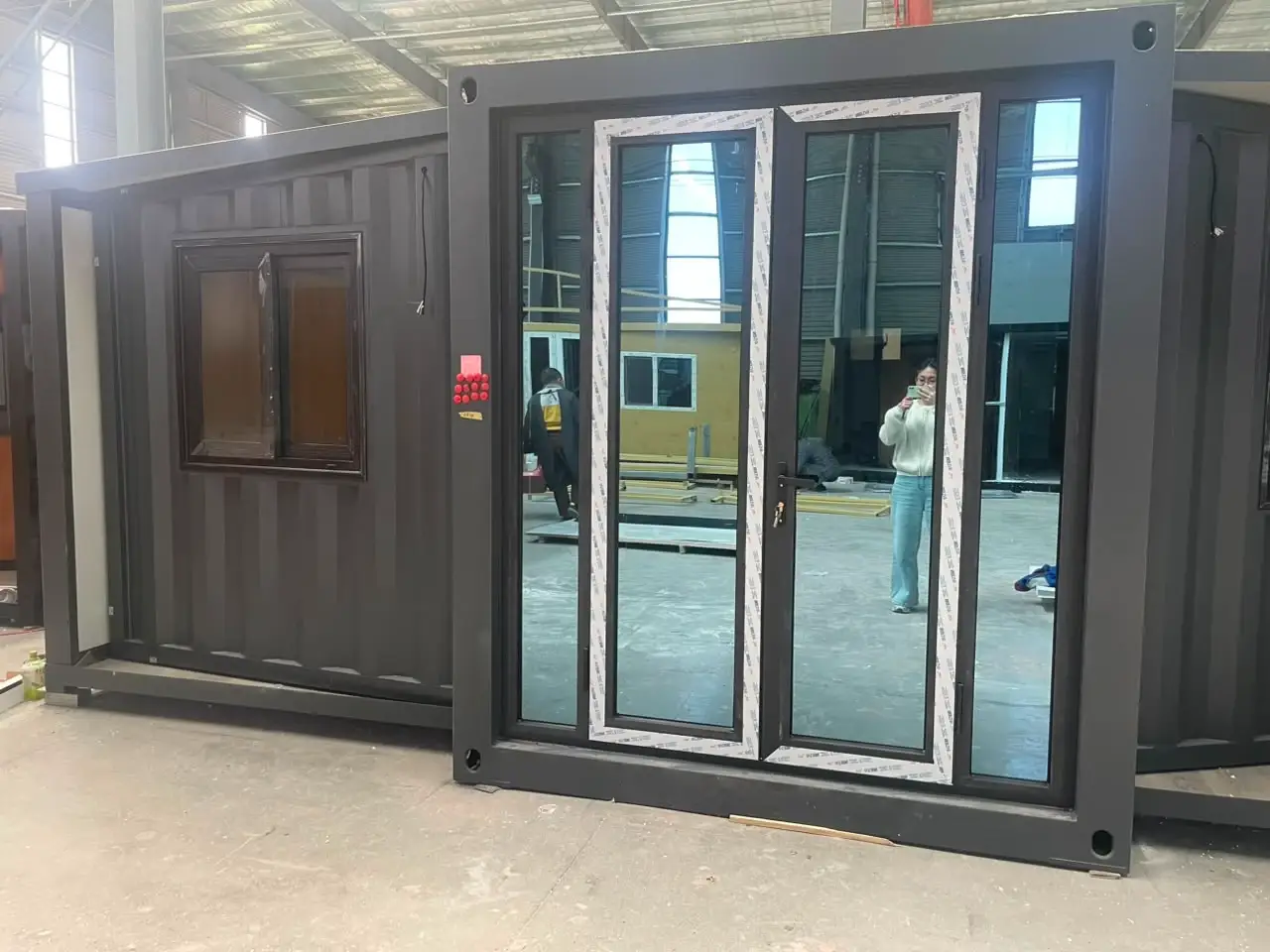 Dark gray container-style modular unit with a glass entrance inside a factory