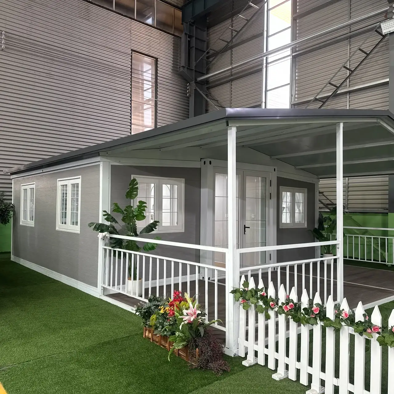 Staged gray modular cottage with a porch, white railings, and showroom landscaping