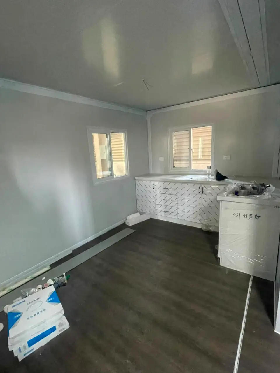 Unfinished modular kitchen with wrapped cabinets, gray flooring, and installation debris