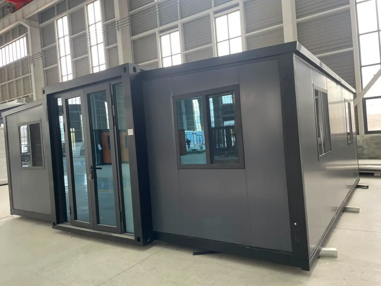 Dark gray expandable modular unit with glass doors and windows inside a factory