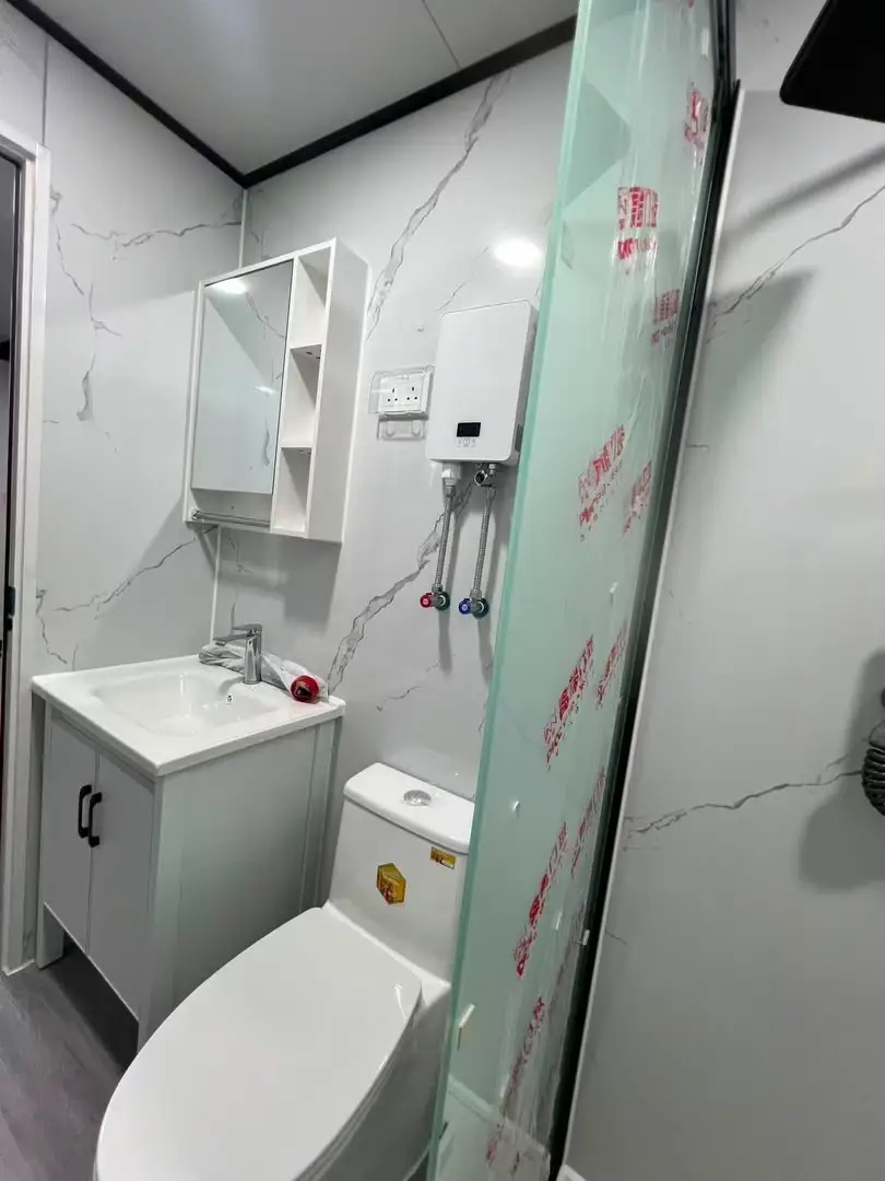 Compact modular bathroom with a vanity, toilet, water heater, and glass partition