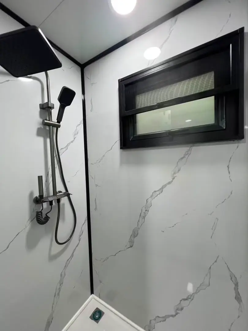 Modular-home shower with black fixtures, marble-look wall panels, and a small window