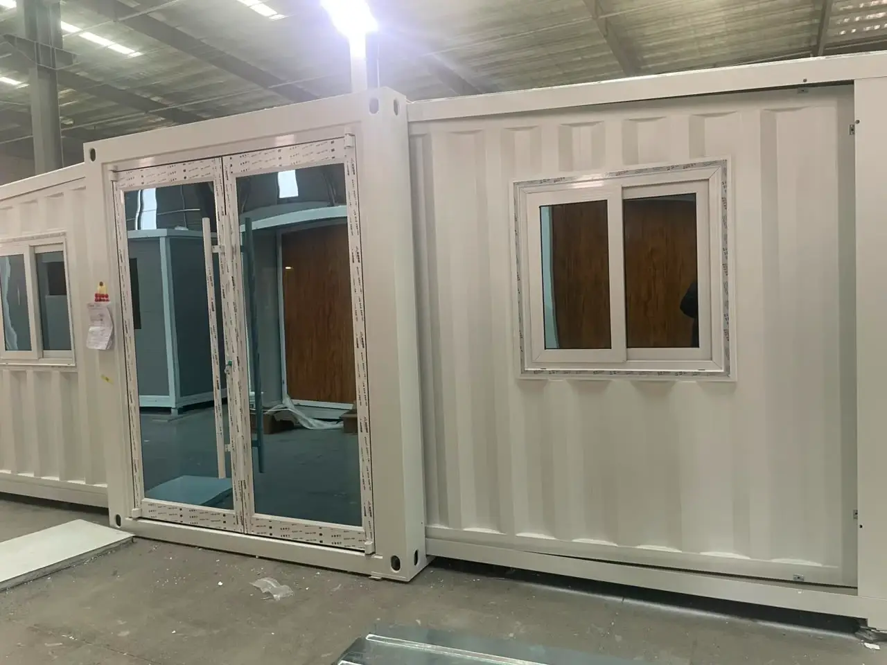 White container-style modular unit with large glass doors and a sliding window