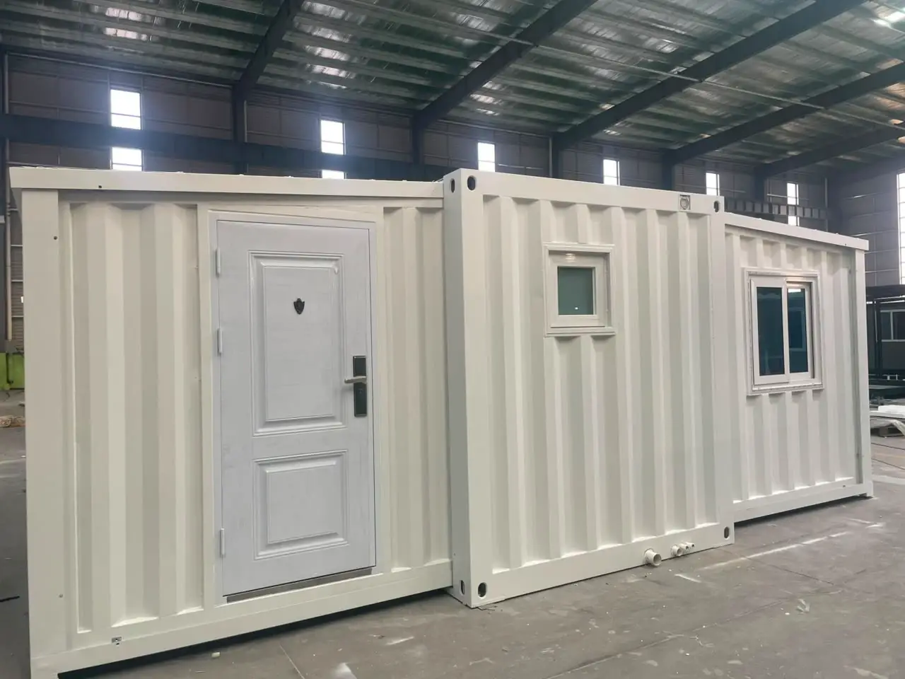 White container-style modular unit with a paneled door and windows inside a warehouse