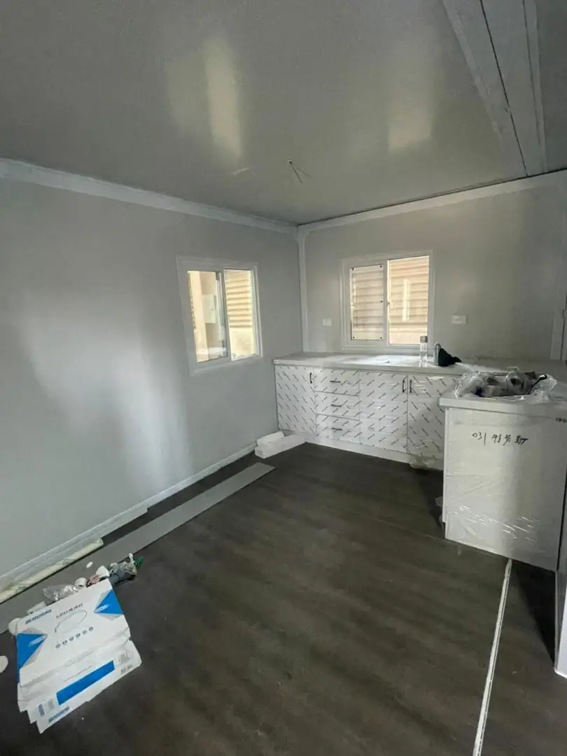 Modular-home kitchen area with wrapped cabinets, dark flooring, and installation materials