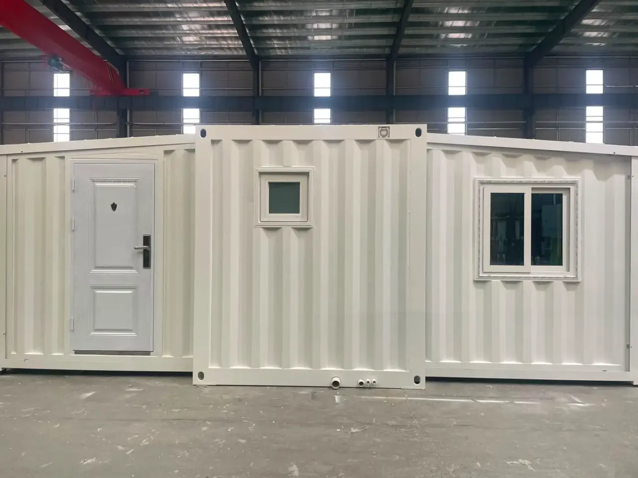 White expandable modular unit with a paneled door and windows on a factory floor
