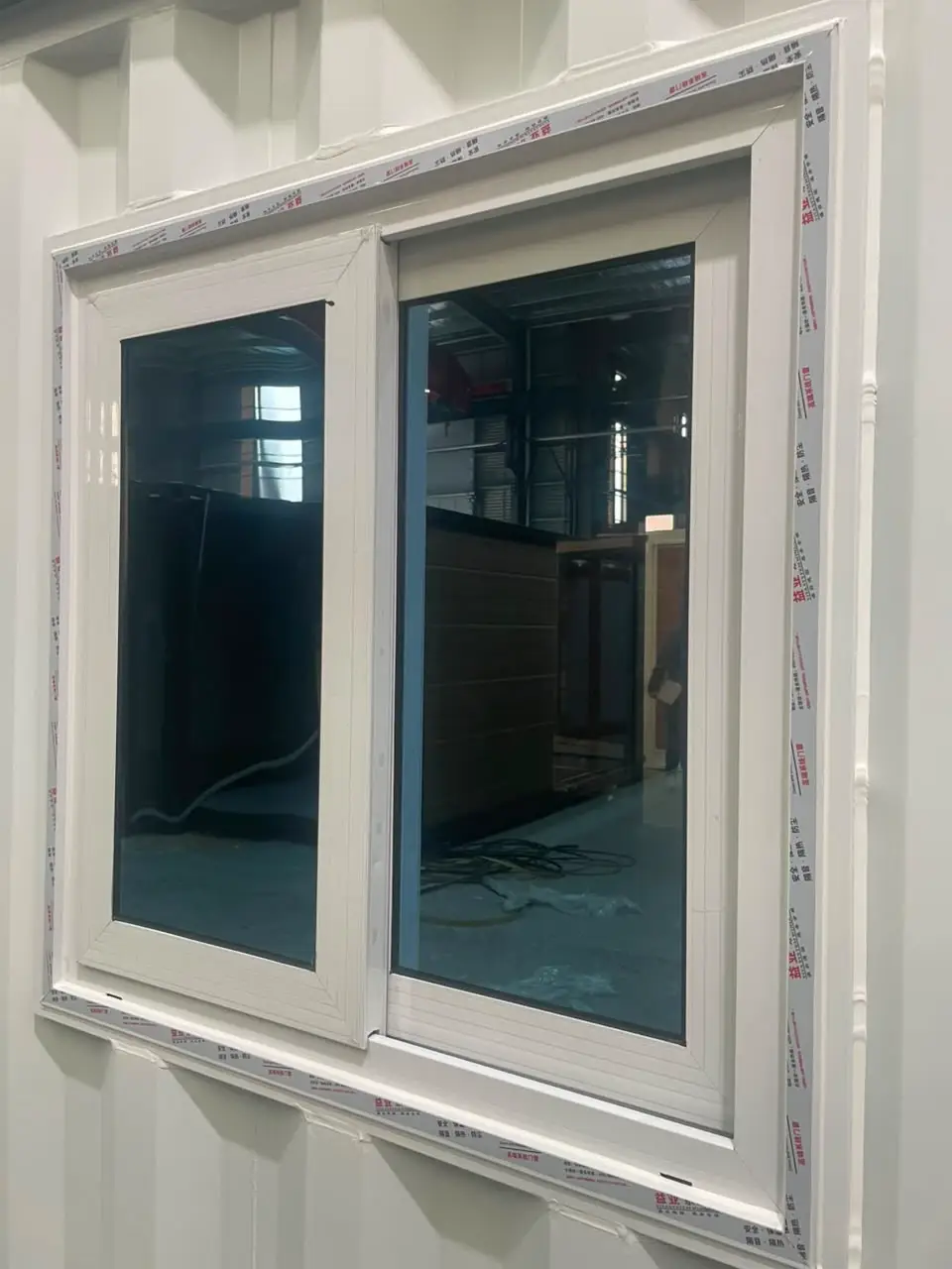 Close view of a white sliding window with protective film in a corrugated modular wall