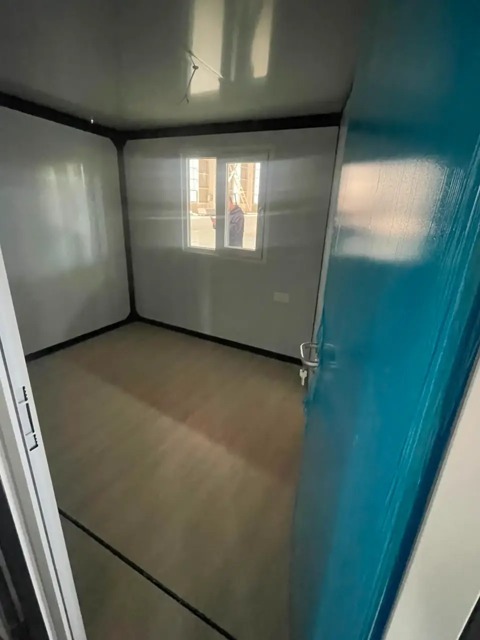 Empty compact modular room with black structural trim and a blue-protected door
