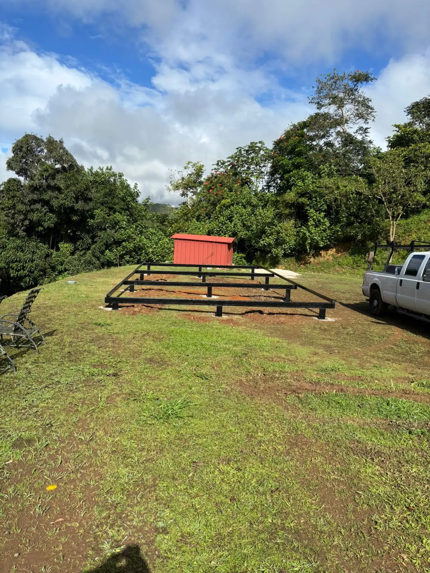 Rectangular black steel foundation frame on a tropical lot beside a utility truck